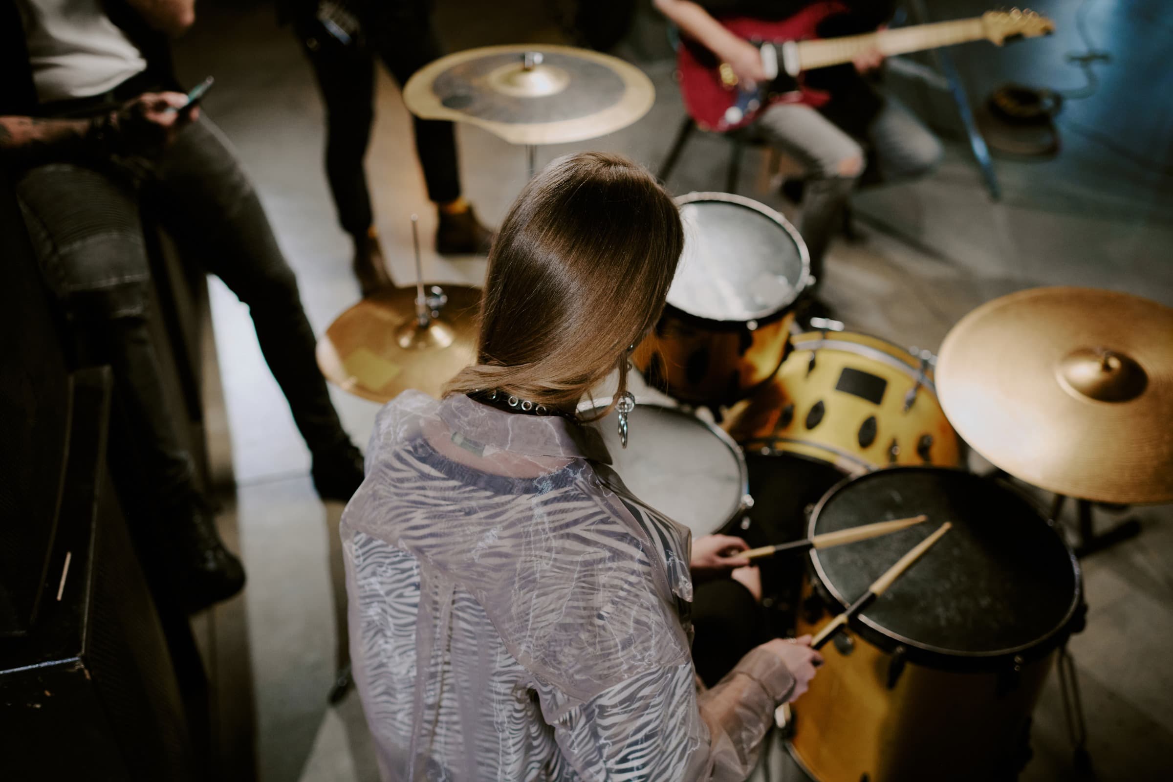 A drummer seen from above mid-rehearsal, with the rest of the band around her